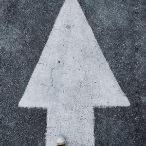 Top-down view of white arrow on asphalt with sneakers stepping forward.